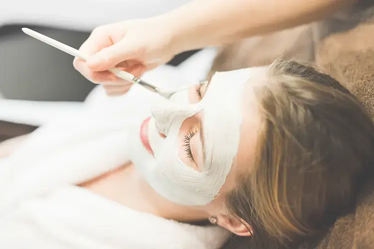 Woman in a bathrobe on a lounger. A facial mask is applied with a brush.
